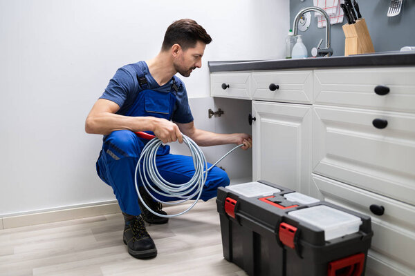 Male Plumber Cleaning Clogged Sink Pipe In Kitchen