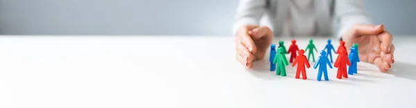 Close Person Hand Protecting Multicolored Pawns Forming Circle White Desk — Stock Photo, Image