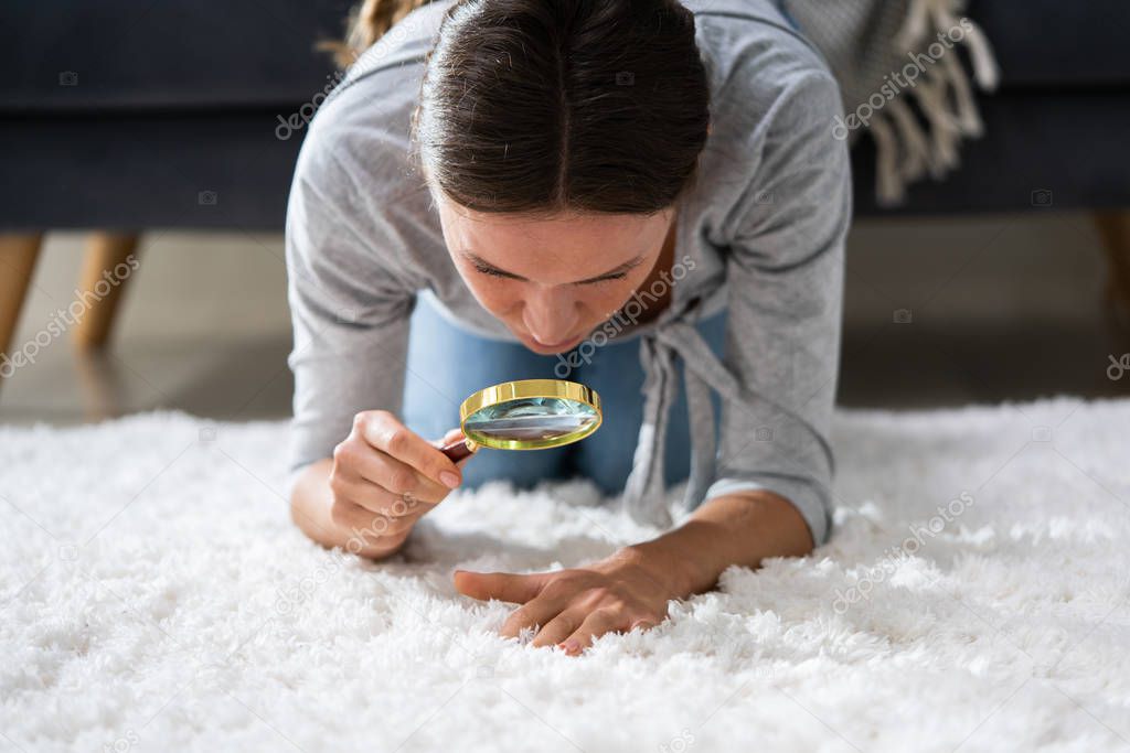 Young Female Looking At Carpet With Magnifying Glass
