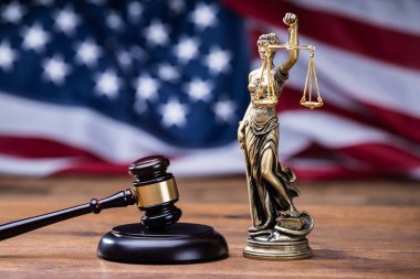 Wooden Gavel With Golden Scales On Table In Front Of US Flag clipart