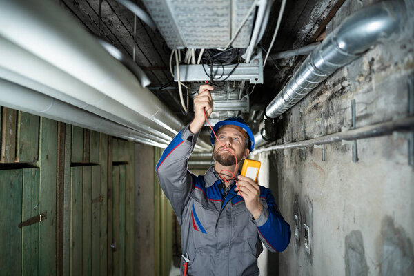 Мужчина носит шляпу, используя мультиметр
 