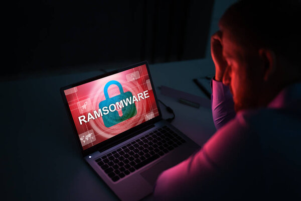 Беспокойный бизнесмен, глядя на ноутбук со словом Ransomware на экране на рабочем месте
