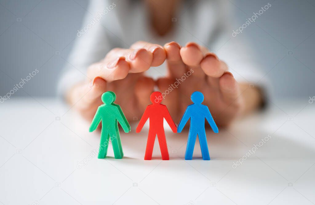 Close-up Of A Person's Hand Protecting Multicolored Pawns Standing In Line Over White Desk