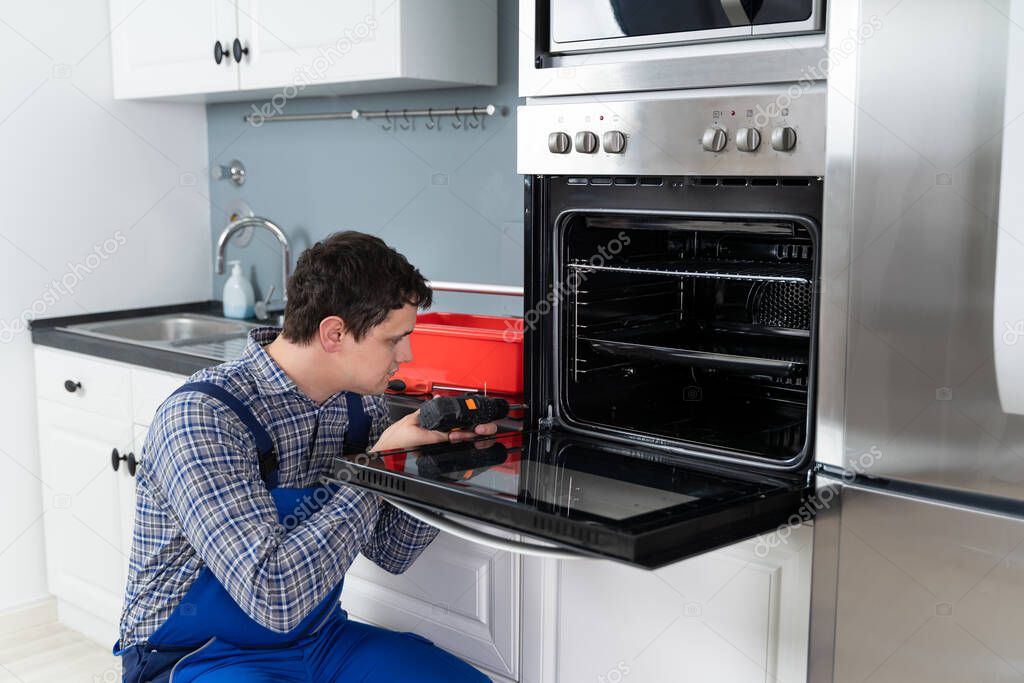 Male Technician In Overall Installing Oven In Kitchen