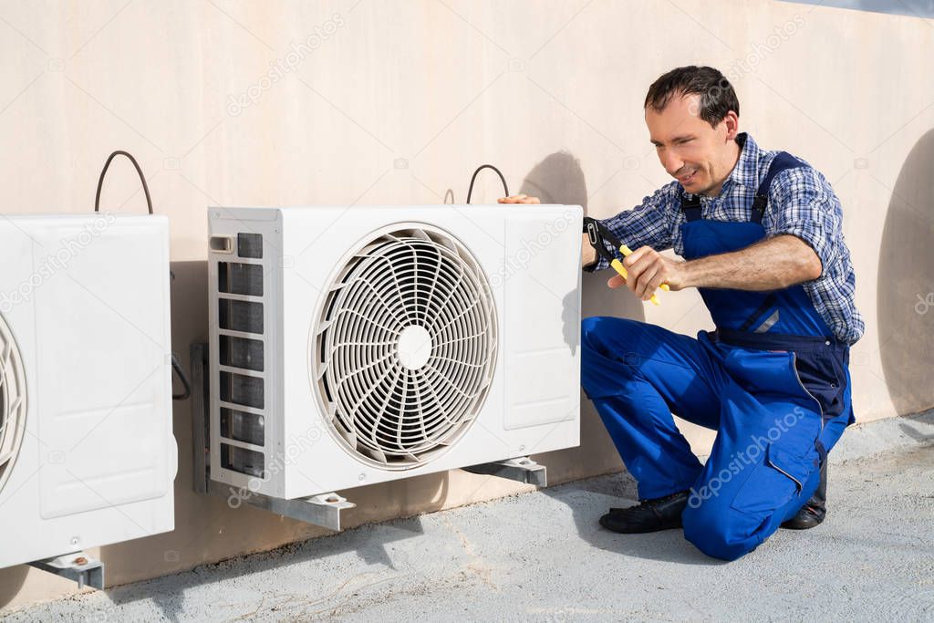 Young Male Technician Repairing Air Conditioning System On Roof