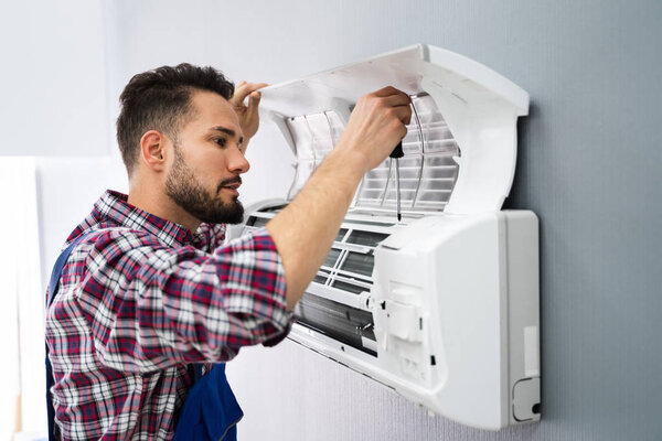 Happy Male Technician Repairing Air Conditioner With Screwdriver