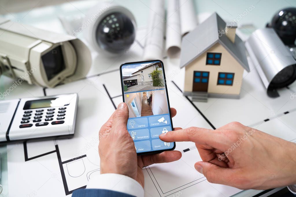 Person Hand Using Home Security System On Mobilephone With On Blueprint With Security Equipment