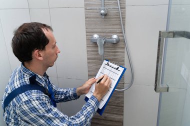 Young Male Plumber Checking Faucet In Shower clipart