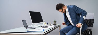 Sandalyeden kalkmak için koltuk değneği kullanan kırık bacaklı bir adam.