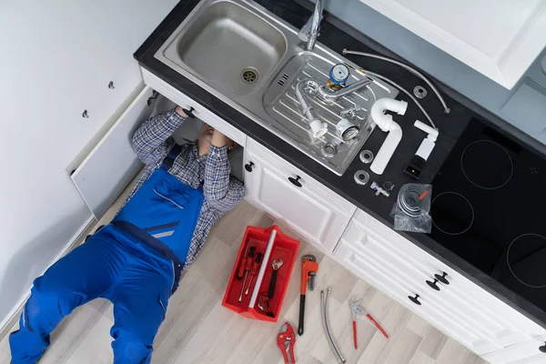 躺在地板修理厨房水槽用可调扳手上的工人 — 图库照片