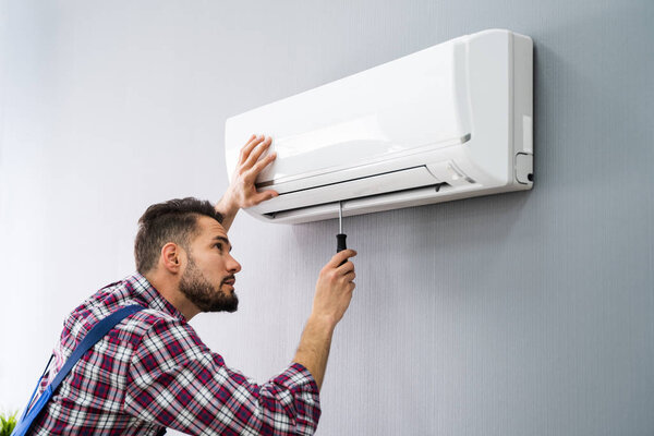 Happy Male Technician Repairing Air Conditioner With Screwdriver