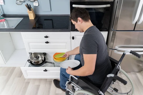 Młody Szczęśliwy Niepełnosprawny Mężczyzna Siedzi Wózku Inwalidzkim Układając Płyty Szufladzie — Zdjęcie stockowe