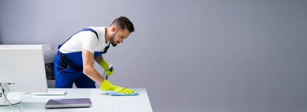 Worker Cleaning Computer Desk With Spray And Sponge