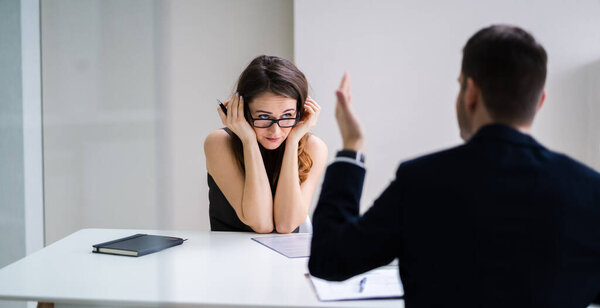 Close-up Of Businessperson Quarreling To Young Businesswoman At Desk