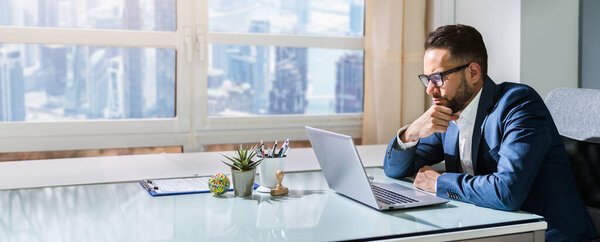 Upset Businessman Sitting In Office With Laptop On Desk