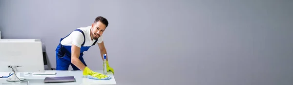 Worker Cleaning Computer Desk With Spray And Sponge