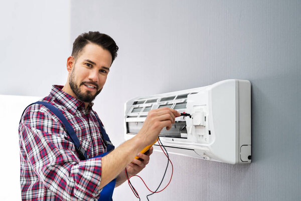 Portrait Of A Mid-adult Male Technician Testing Air Conditioner With Digital Multimeter