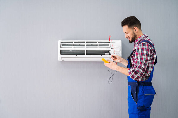 Portrait Of A Mid-adult Male Technician Testing Air Conditioner With Digital Multimeter