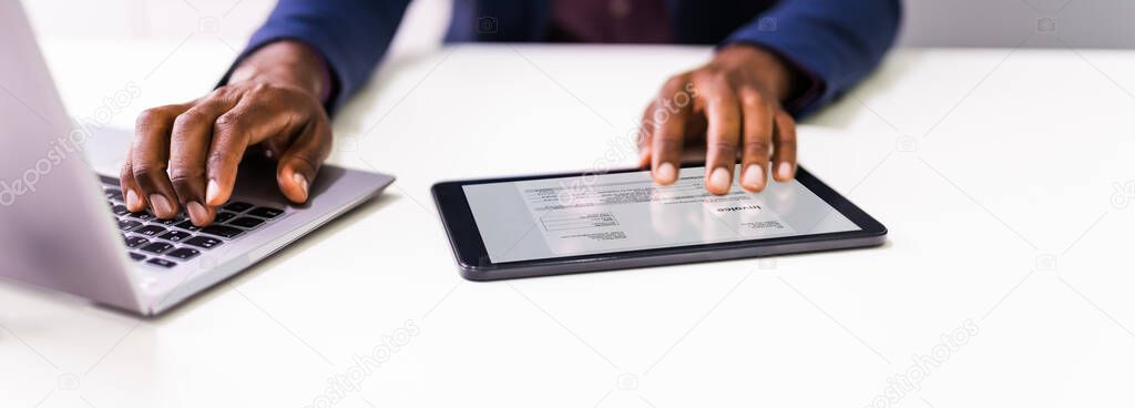 Close-up Of A Businessperson's Hand Analyzing Bill On Digital Tablet Over Desk