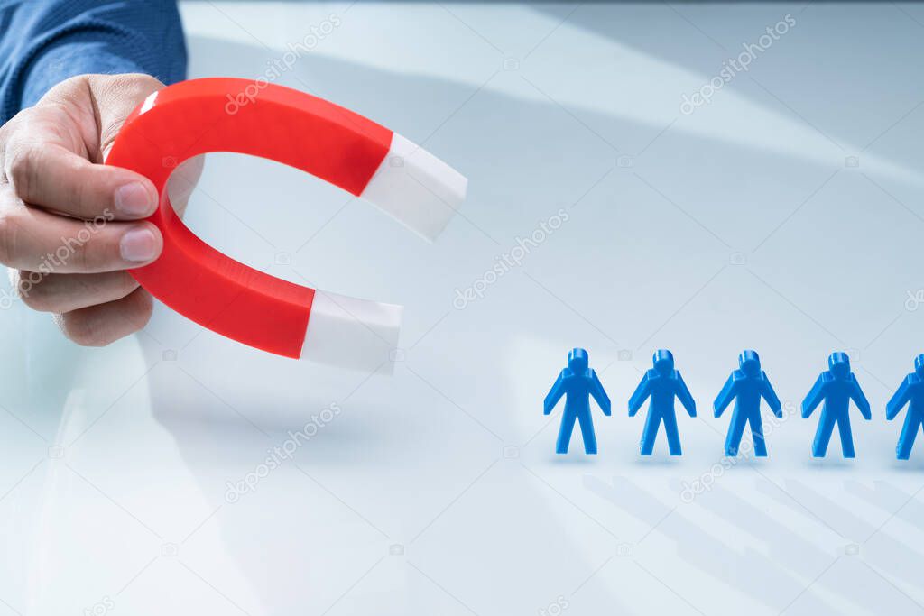 Businessman's Hand Attracting Blue Team With Horseshoe Magnet On White Background