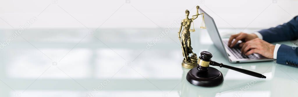 Close-up Of A Businessperson's Hand Using Laptop With Gavel On Desk