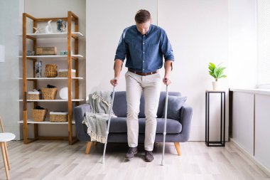 Yürümek için koltuk değneği kullanan engelli genç adam.