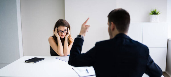 Close-up Of Businessperson Quarreling To Young Businesswoman At Desk