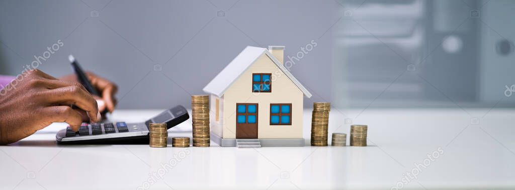 Businessman Calculating Tax By Model House And Coins