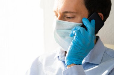 Koronavirüs karantinasında maskeli ve eldivenli adam cep telefonu kullanıyor.