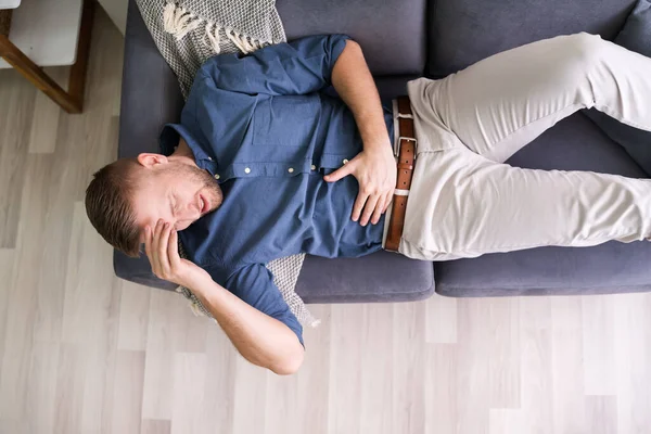 ソファの上に横たわる胃の痛みに苦しむ男 — ストック写真