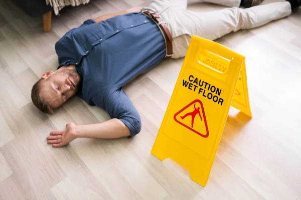 Mature Man Falling On Wet Floor In Front Of Caution Sign At Home