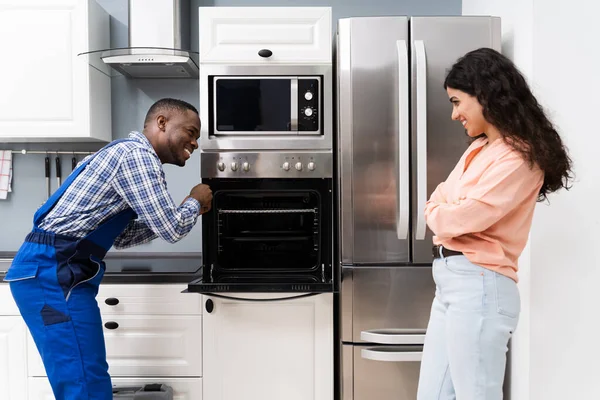 Woman Looking At Male Worker Repairing Oven Appliance In Kitchen Room