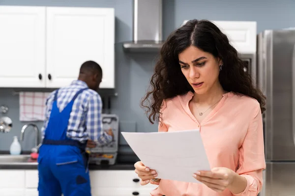 Joven Mujer Frustrada Mirando Factura Caro Portapapeles Con Fontanero Pie — Foto de Stock