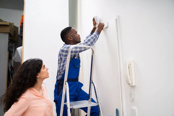 Happy Woman Looking Electrician Installing Security System Motion Detector Wall — Stock fotografie