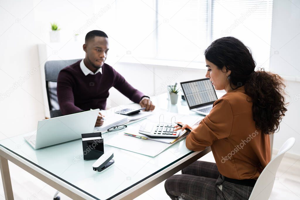 Close-up Of Two Businesspeople Calculating Financial Statement At Desk