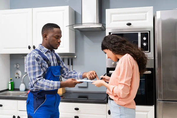 台所に立つ配管工の前で笑顔の顧客女性のサインアプライアンス修理請求書 — ストック写真