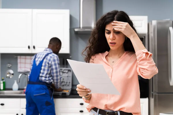 Joven Mujer Frustrada Mirando Factura Caro Portapapeles Con Fontanero Pie — Foto de Stock