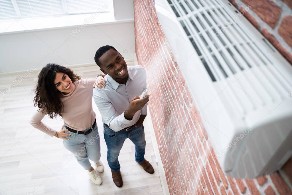 Portrait Of Happy Couple Holding Remote Control Air Conditioner
