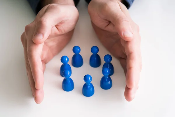 Close Person Hand Protecting Multicolored Pawns Forming Circle White Desk — Stock Photo, Image