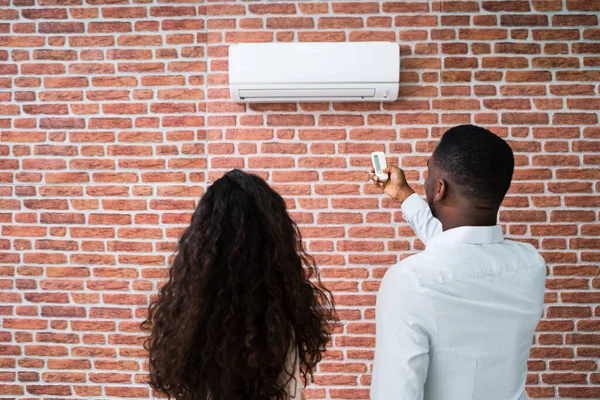 Casal Jovem Feliz Ajustando Temperatura Condicionador Por Remoto — Fotografia de Stock