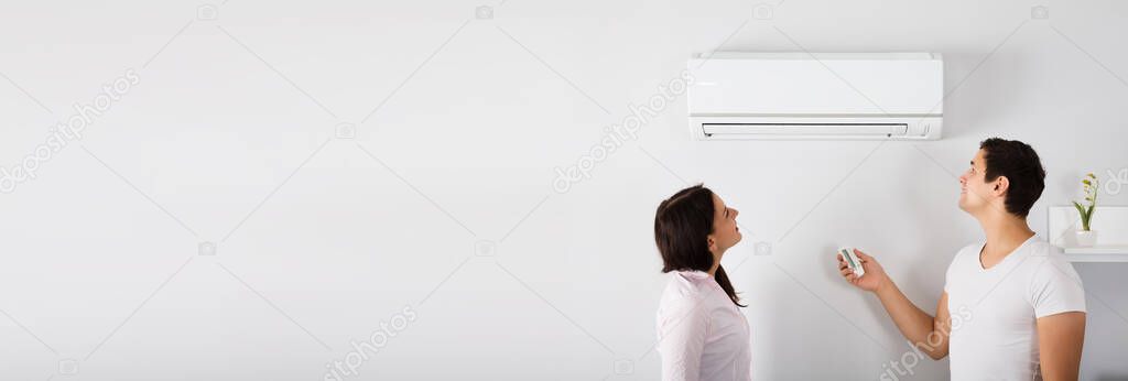 Couple Operating Air Conditioner In Living Room At Home