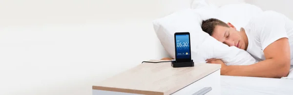 Alarm Clock On Mobile Phone. Sleepy Man Sleeping Near Smartphone