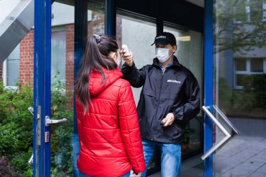 Güvenlik görevlisi binanın girişindeki sıcaklığı kontrol ediyor.