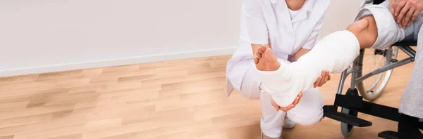 Doctor Looking At Patient Leg Cast With Broken Bone Injury