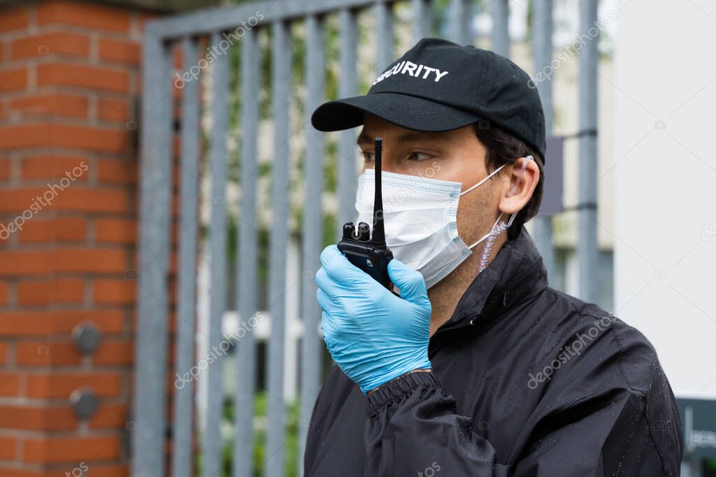 Security Guard In Face Mask Talking On Walkie Talkie