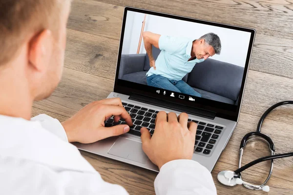 Doctor In Video Conference Call With Patient Having Back Pain