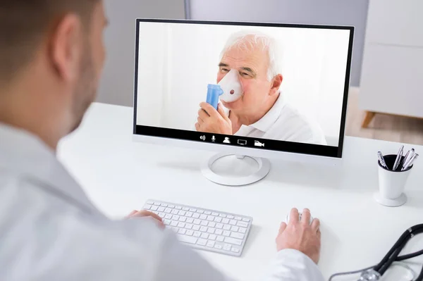Doctor In Video Conference Call With Senior Patient Using Oxygen Nebulizer
