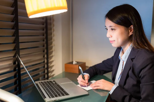 Businesswoman writing on the note with laptop computer