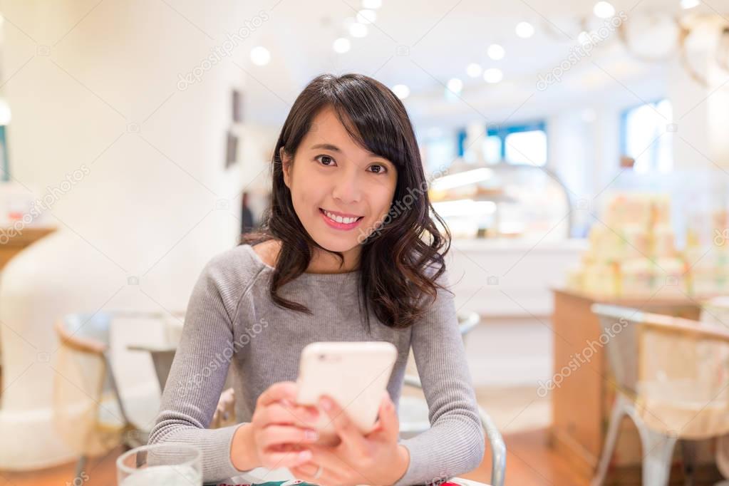 Woman using cellphone in cake shop