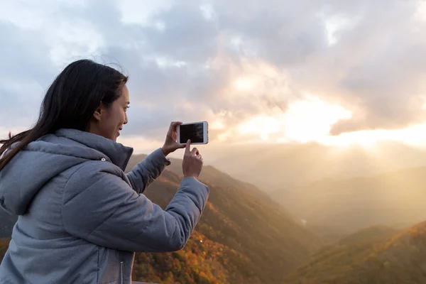 Mujer usando el teléfono celular para tomar fotos durante el atardecer — Foto de Stock